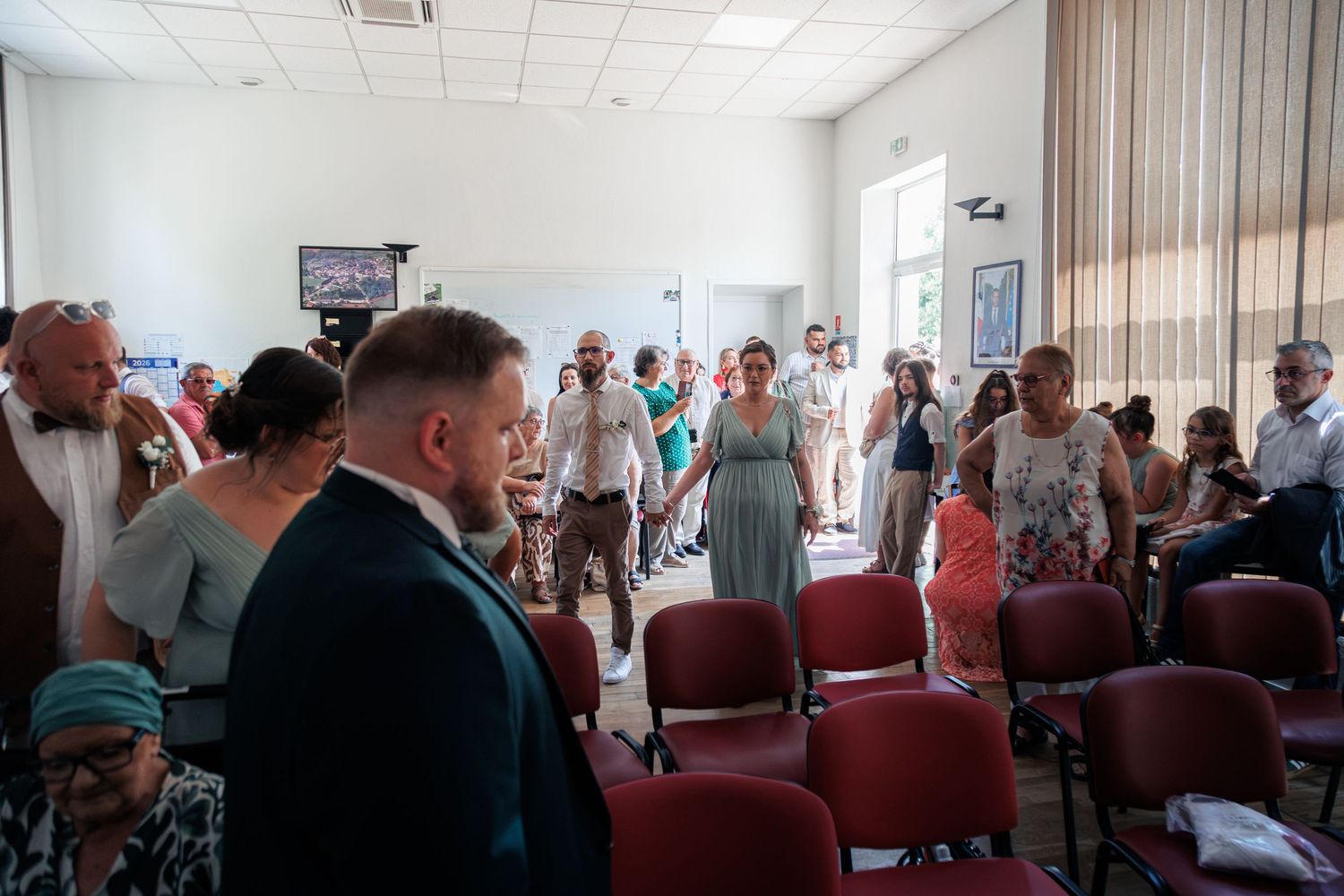 Wedding guests mingling inside a bright room with red chairs during a French civil ceremony celebration.