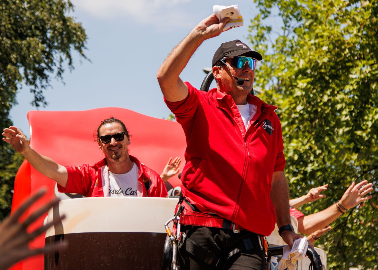 Performers in red attire energetically entertain the crowd from atop a parade float.