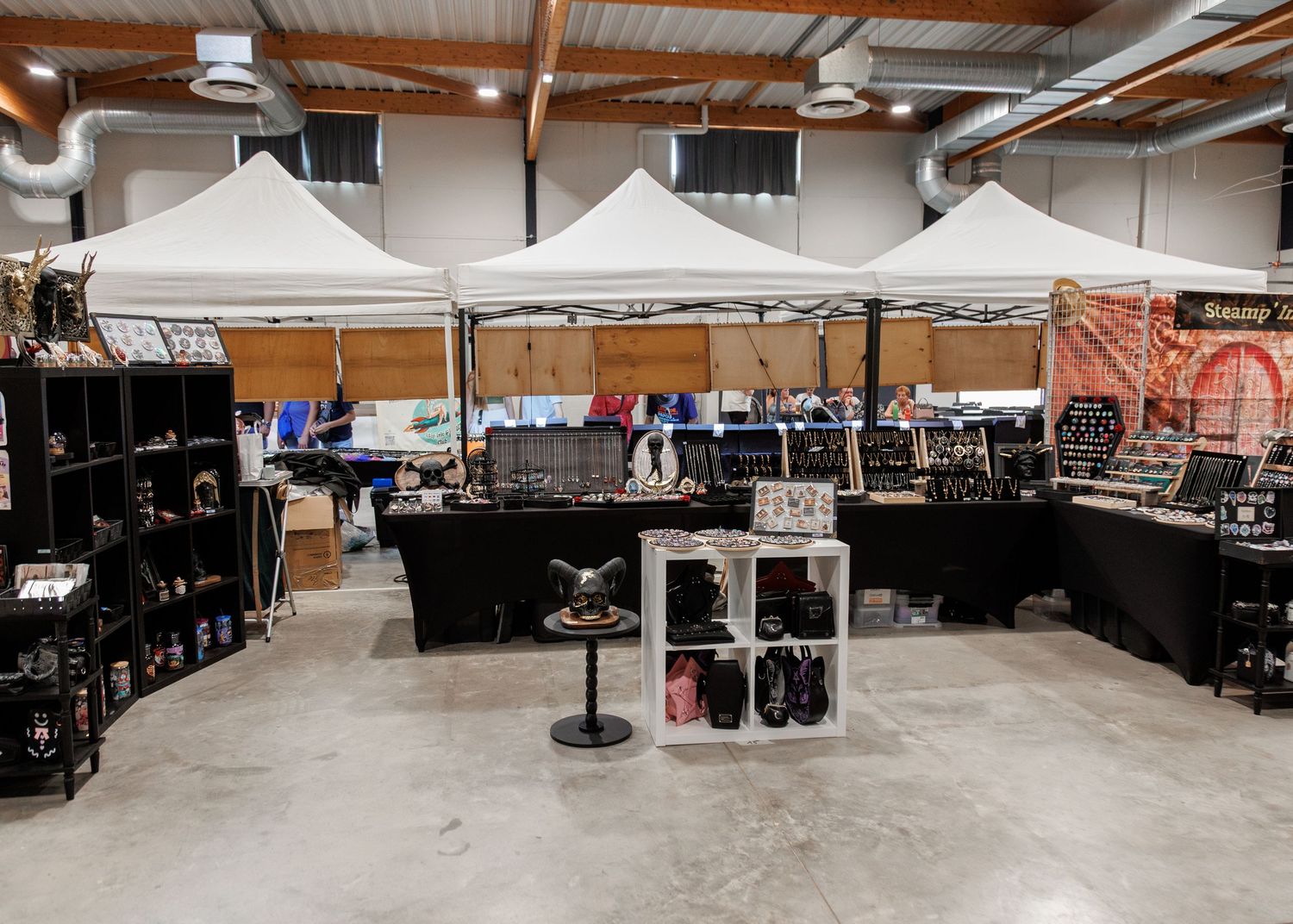 Indoor market vendor booth with white canopy tents displaying jewelry and accessories on black shelving units.