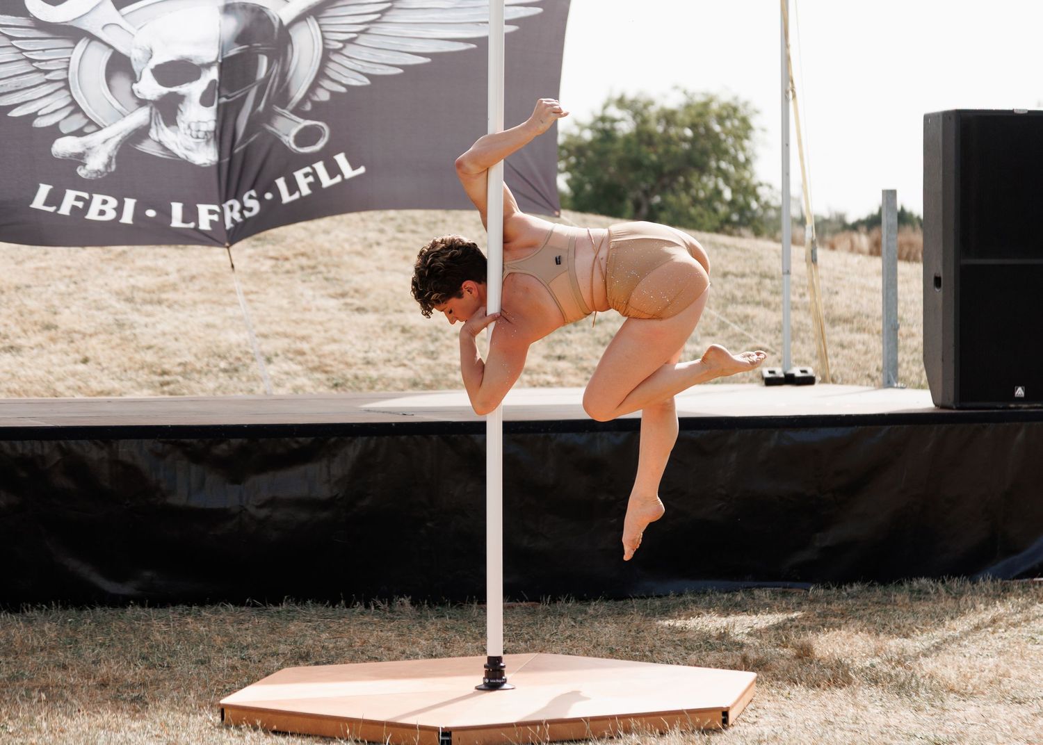 Flexible pole dancer performing an impressive aerial split on an outdoor stage at a festival event.