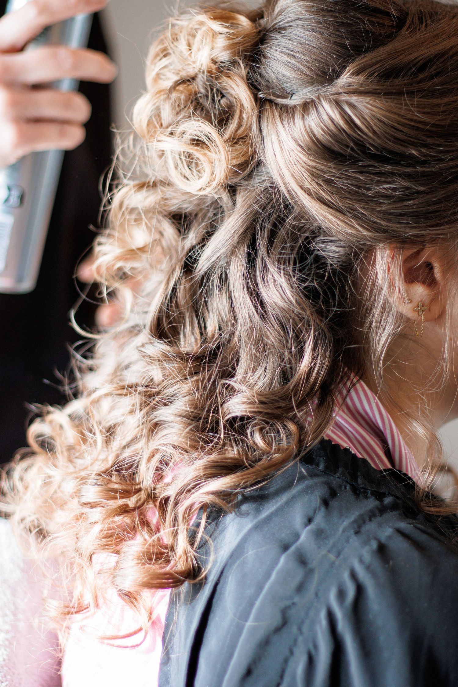 Close-up of elegant half-up curly hairstyle being finished with hairspray by a professional stylist.
