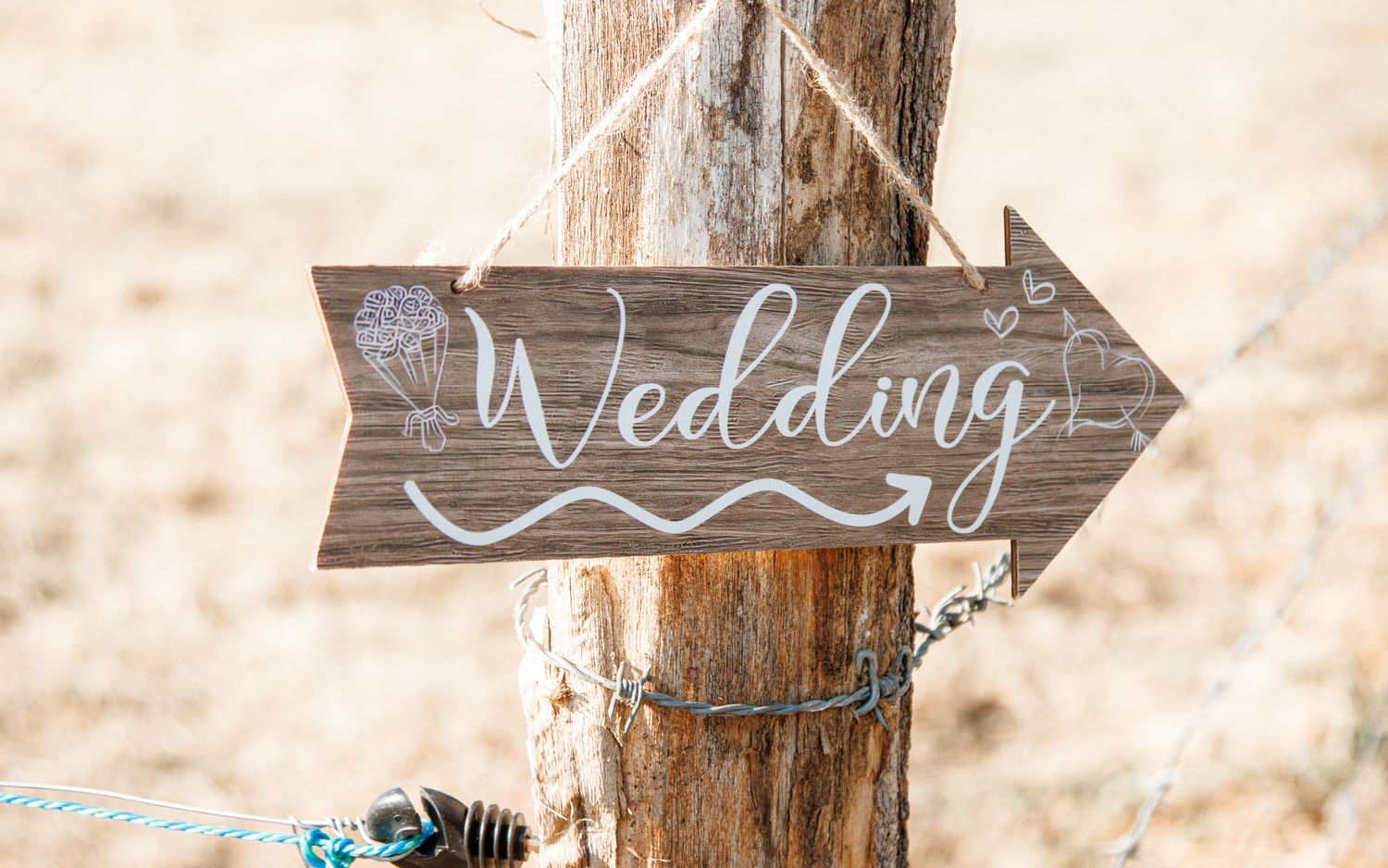 Rustic wooden arrow wedding sign with white calligraphy lettering mounted on natural log post in outdoor setting.