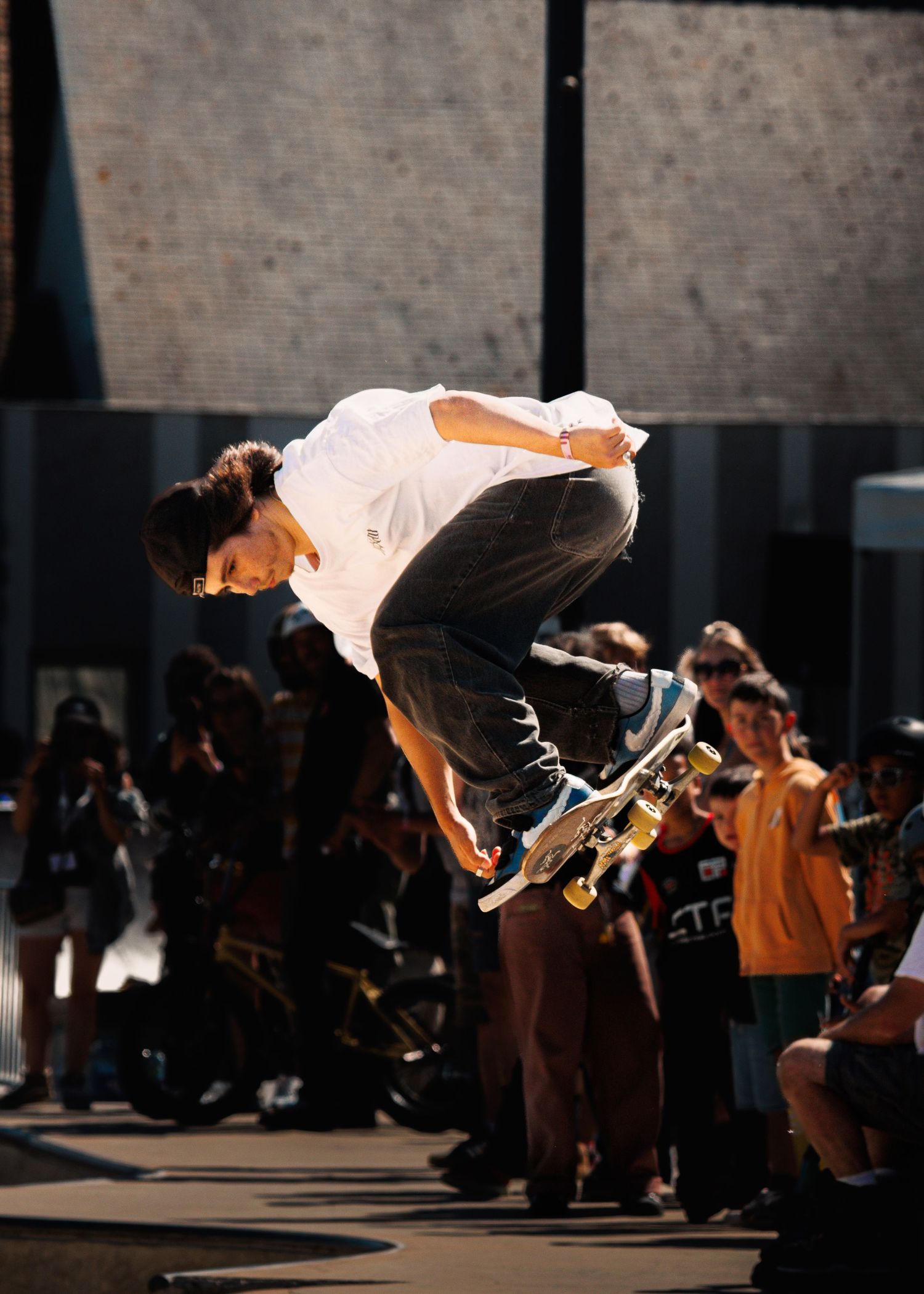 Skateboarder performing aerial trick at outdoor skate competition with crowd watching.
