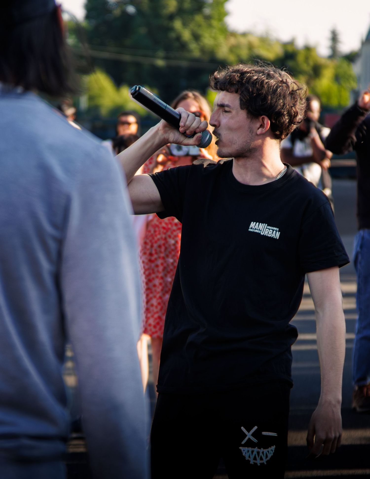 Performer in black t-shirt drinks from bottle during outdoor summer event.