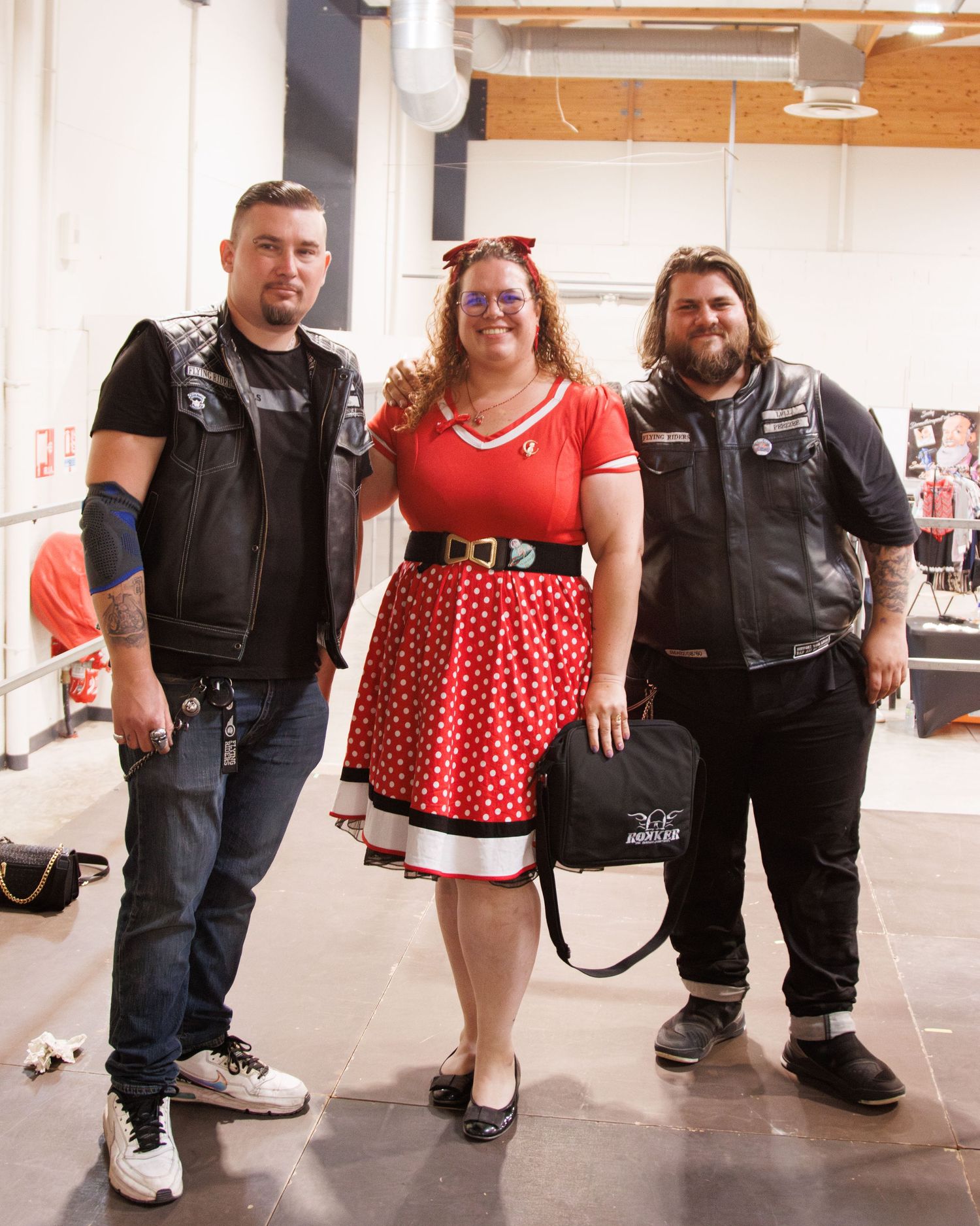 A group wearing black leather vests pose indoors near motorcycle branding.