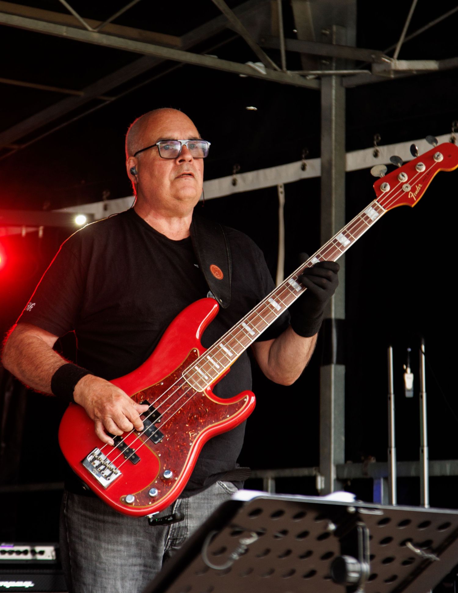 Musician playing a red bass guitar on stage under dramatic lighting.