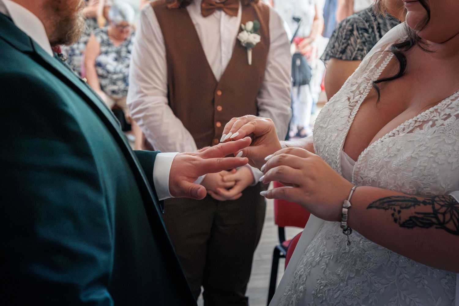 Close-up of bride and groom exchanging rings during wedding ceremony, bride has floral tattoo on wrist.
