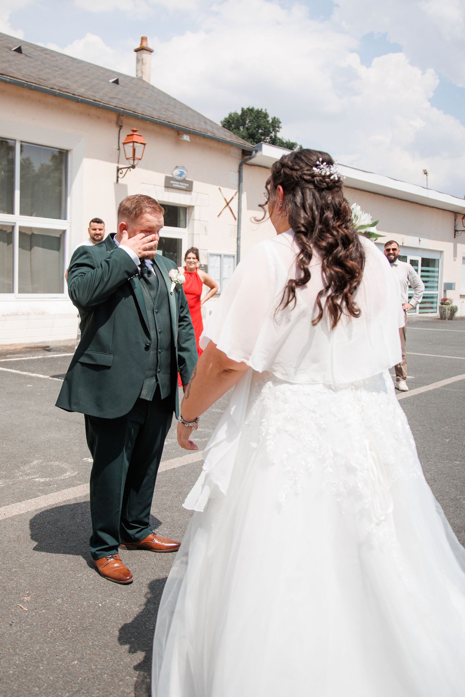 Emotional groom wiping tears as bride in white wedding dress approaches during outdoor first look ceremony.