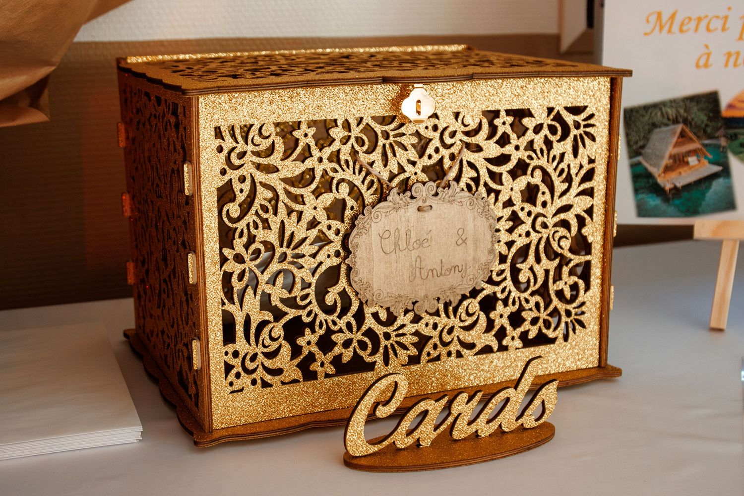Ornate gold laser-cut wooden wedding card box with floral design and Cards sign on decorated table.