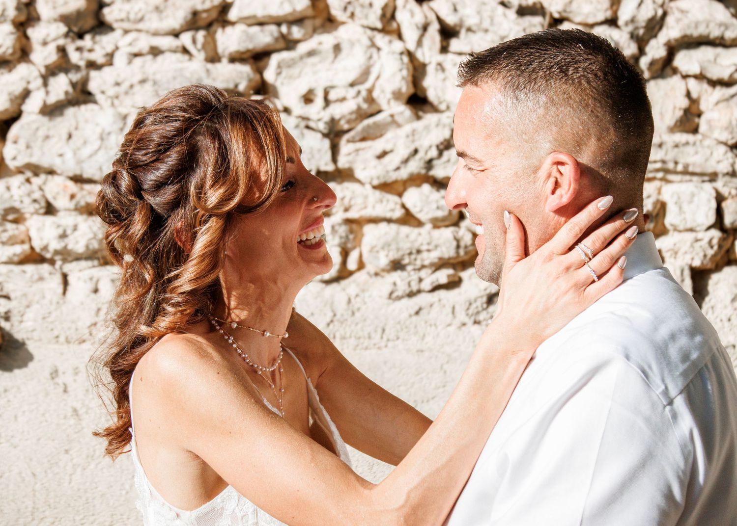 A bride and groom share tender moments together against a rustic stone wall background during their wedding day.