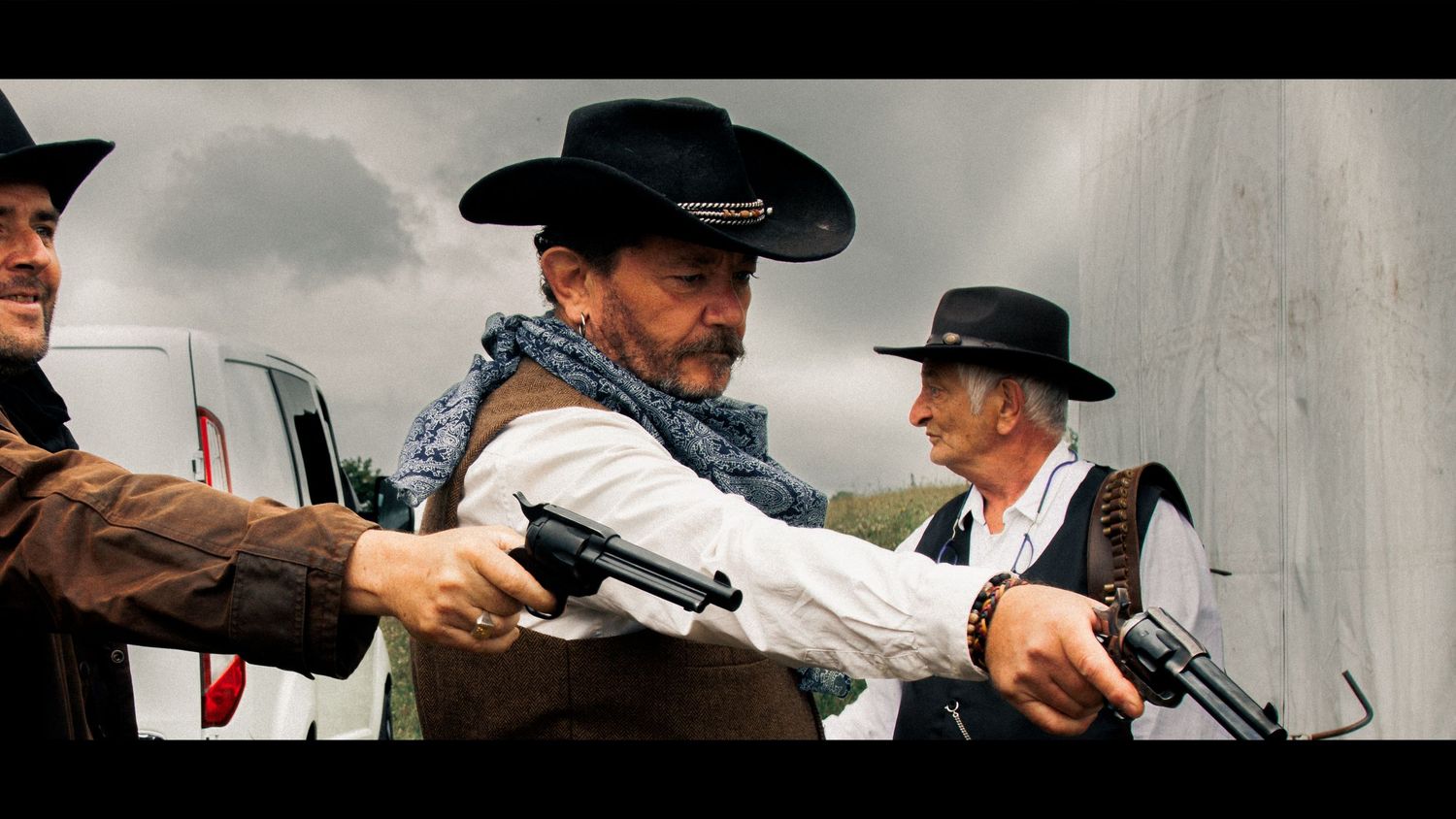 Cowboys in period dress point revolvers during an action scene against cloudy sky.