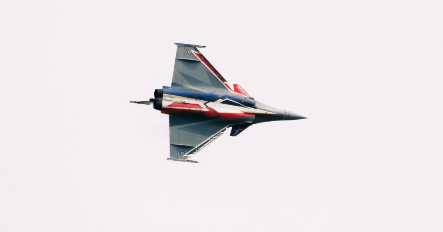 Modern fighter jet aircraft performing aerial maneuver against white sky.