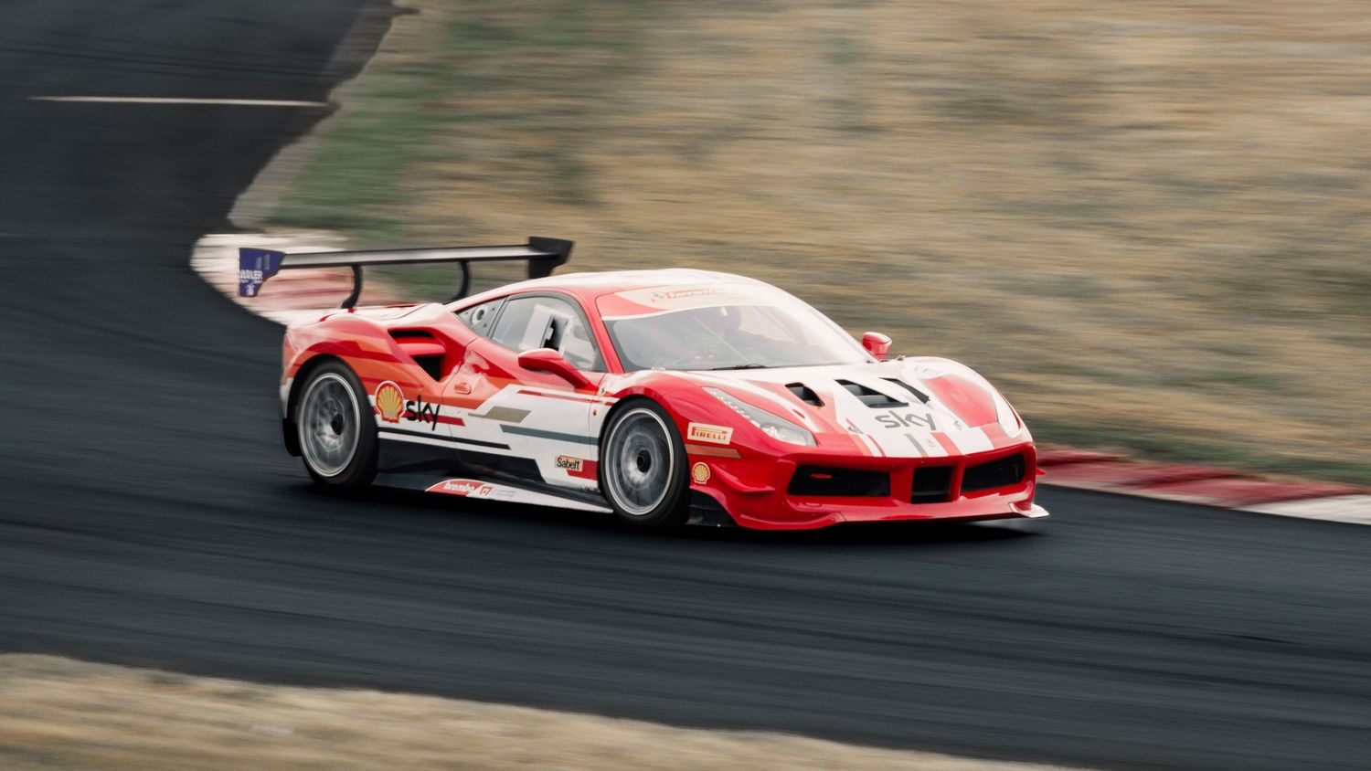 Red Ferrari 488 GT3 race car speeds through a racetrack corner with motion blur.