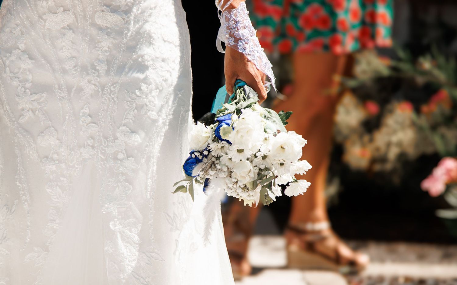 Detail shot of a white lace wedding dress and bouquet with blue and white flowers.