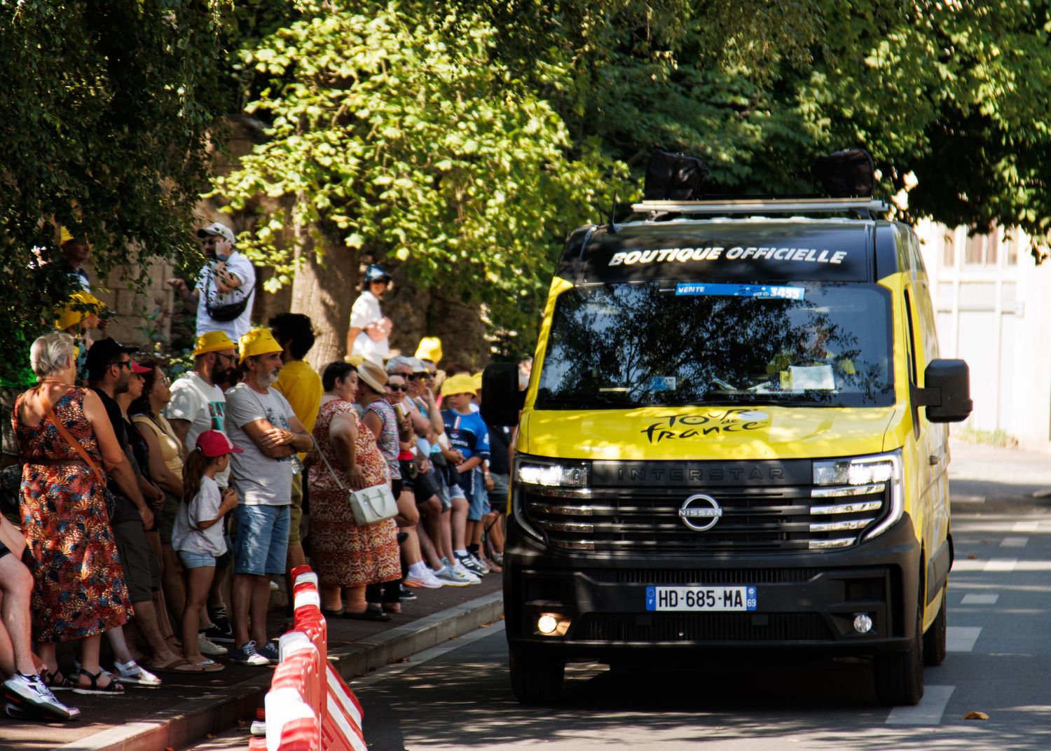 Vehicles including a black van drive down a street lined with spectators during a public event.