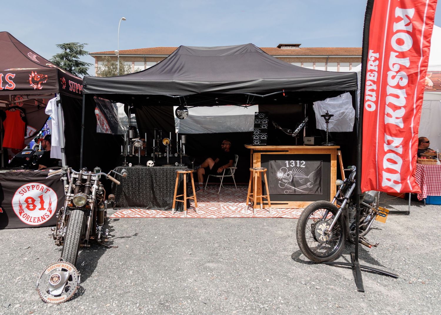 Outdoor motorcycle vendor booth with custom bikes displayed under a black tent at a HDN Kustom rally event.
