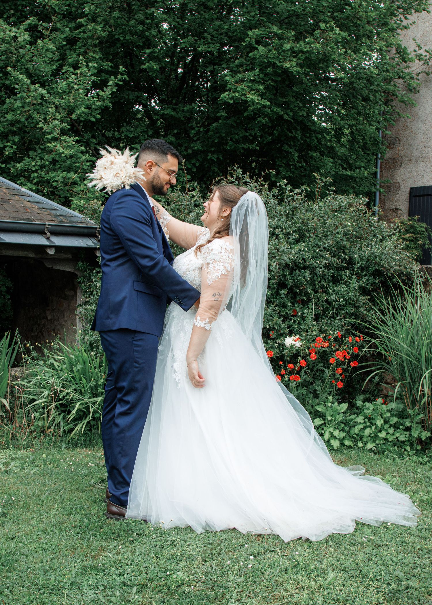 A bride and groom share a romantic moment in a lush garden, with the bride in a white gown and groom in a navy suit.