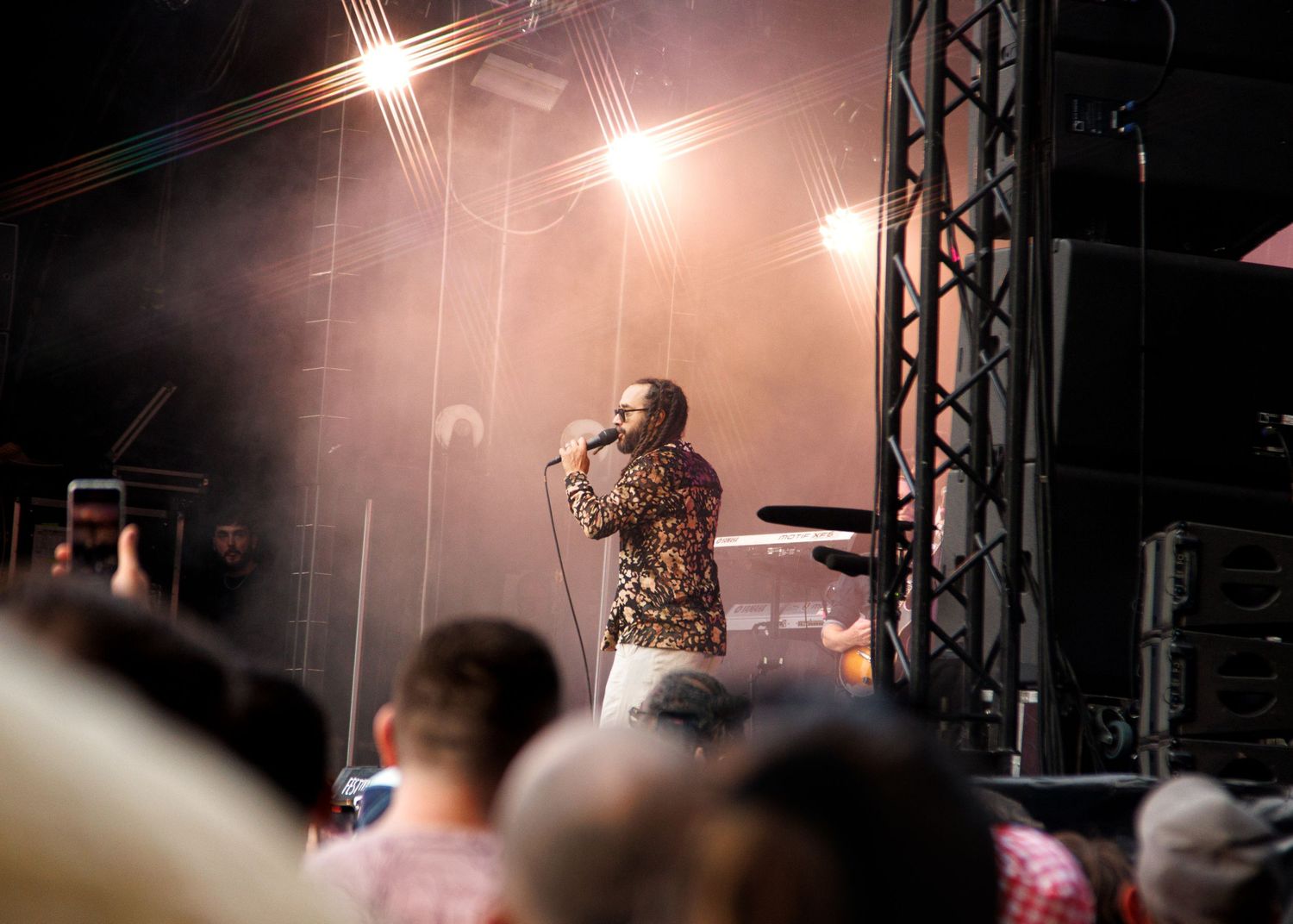 Singer performing on stage in a sequined jacket under bright spotlights at an outdoor concert.