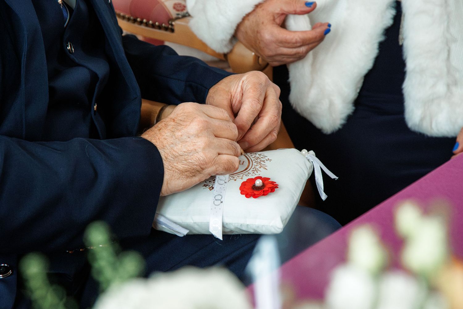 Hands carefully sewing a small red button onto white fabric during a detailed crafting session.