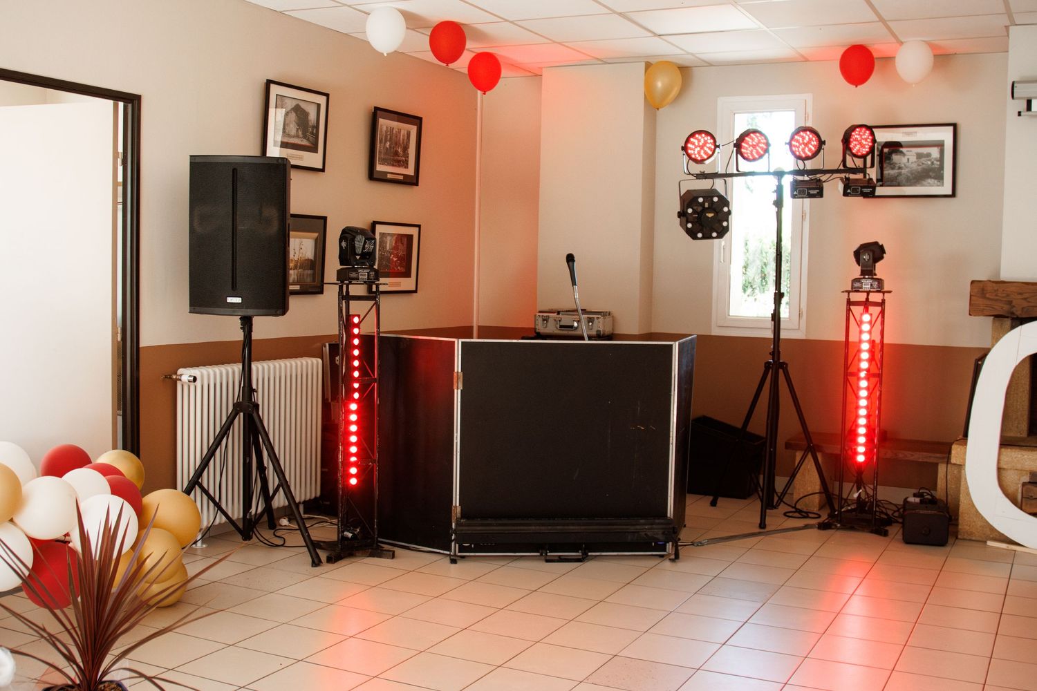 Wedding DJ setup with illuminated speaker stands, balloons, and lighting equipment in reception hall.