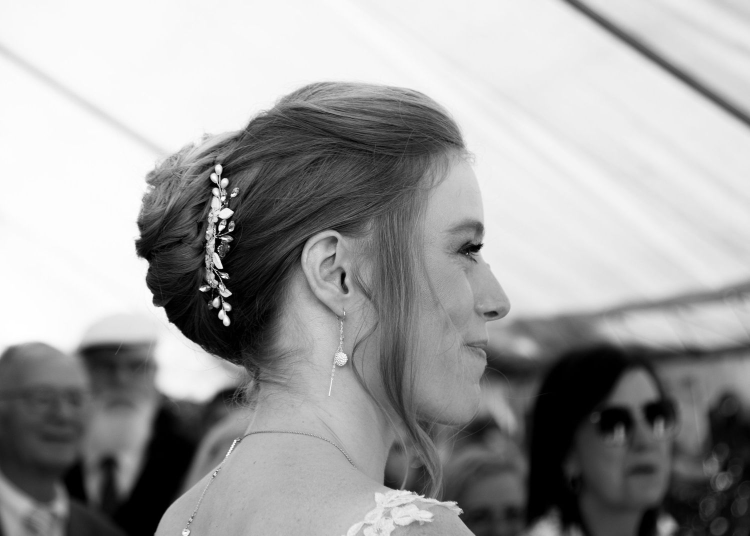 Black and white close-up of bride's elegant updo hairstyle with decorative hair accessory and pearl earring.