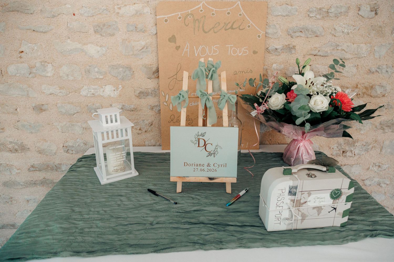 Wedding welcome table with monogram easel, white lantern, vintage suitcase, and floral bouquet decor.