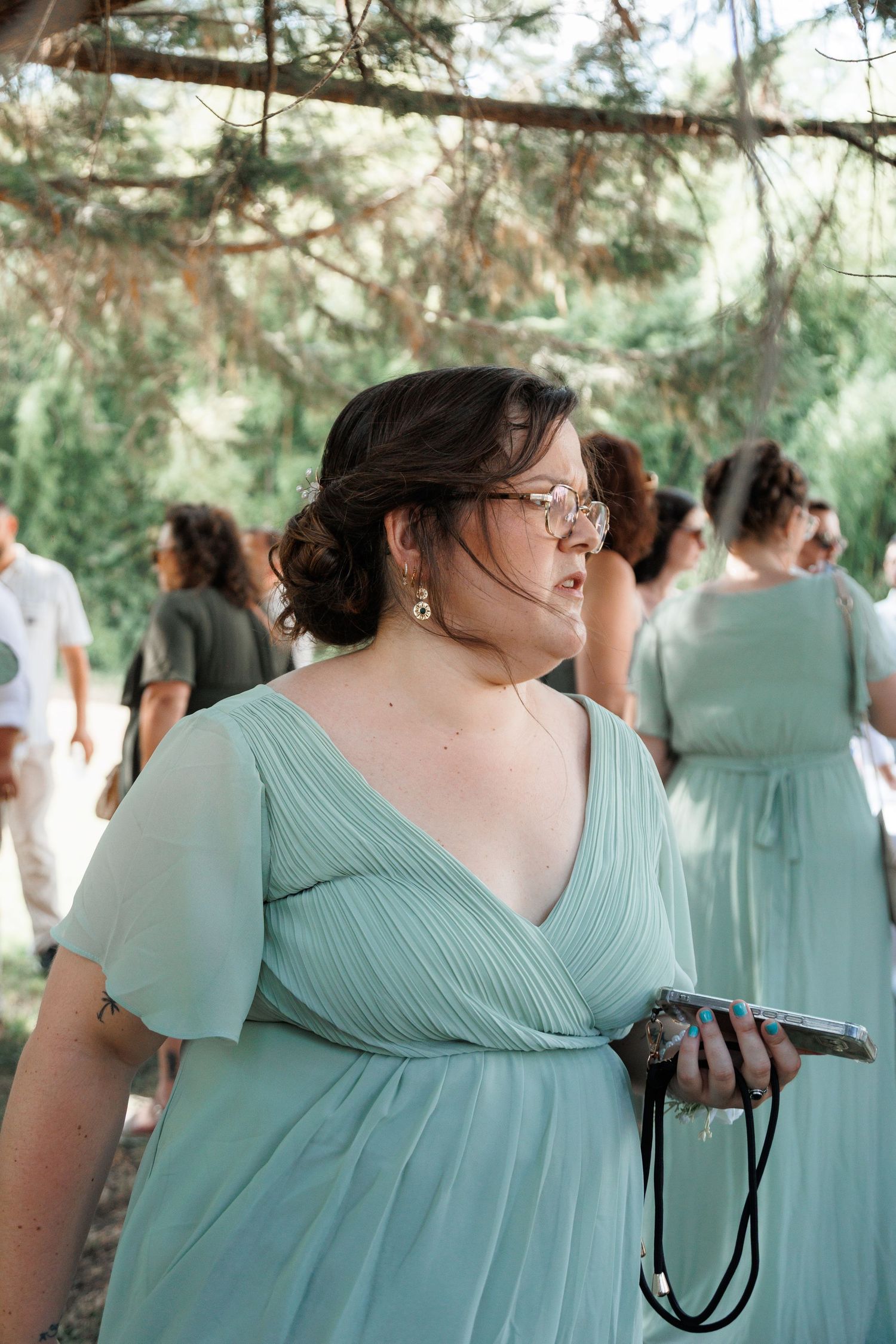 Bridesmaid in mint green dress holding phone at outdoor wedding ceremony.
