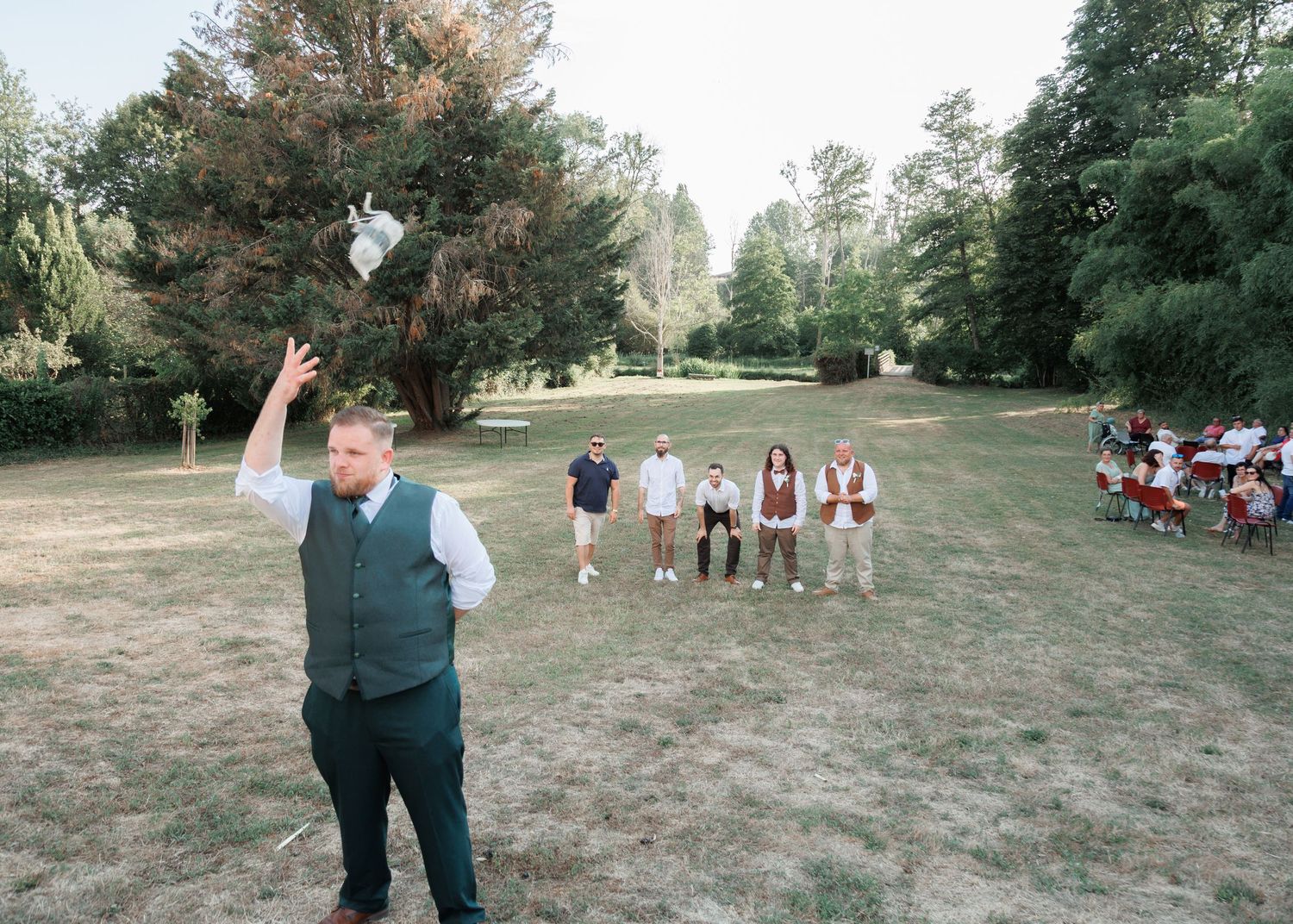 Man tossing an object in the air during outdoor wedding lawn games with guests watching.