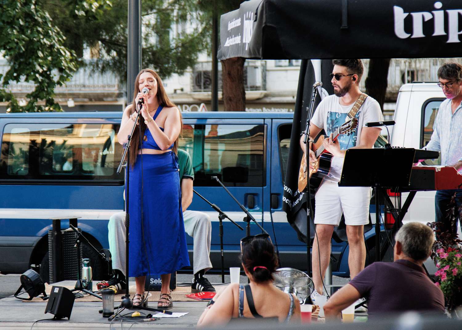Band performing at outdoor festival with singer in blue dress.