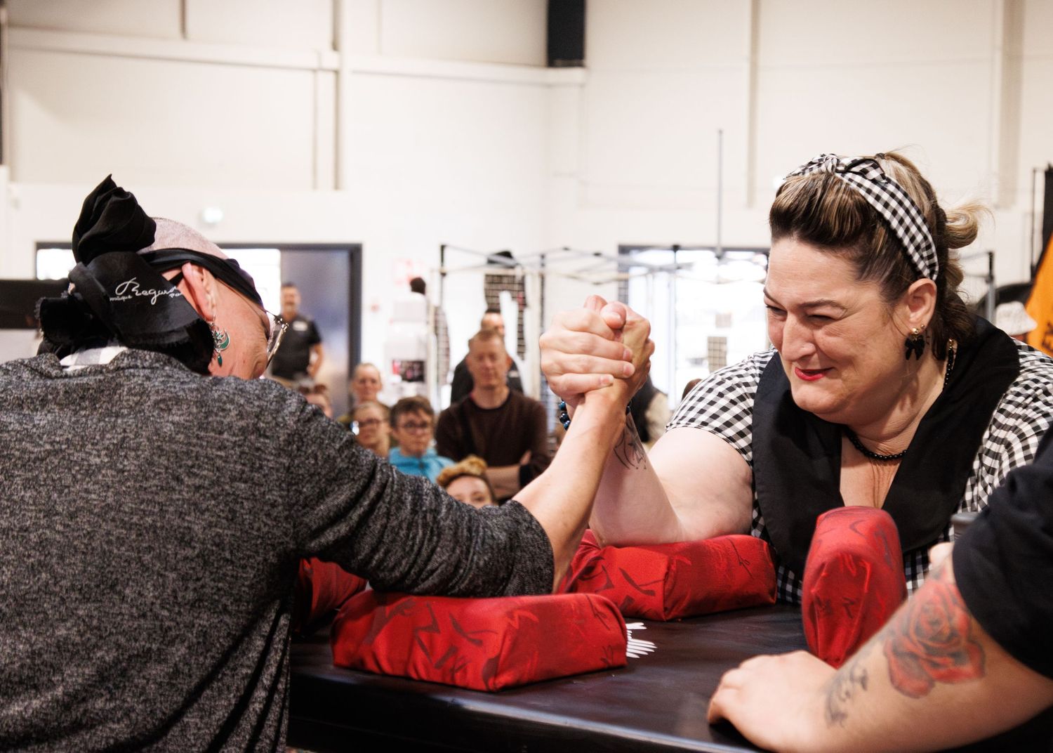 Intense arm wrestling competition between two competitors with spectators watching in background.