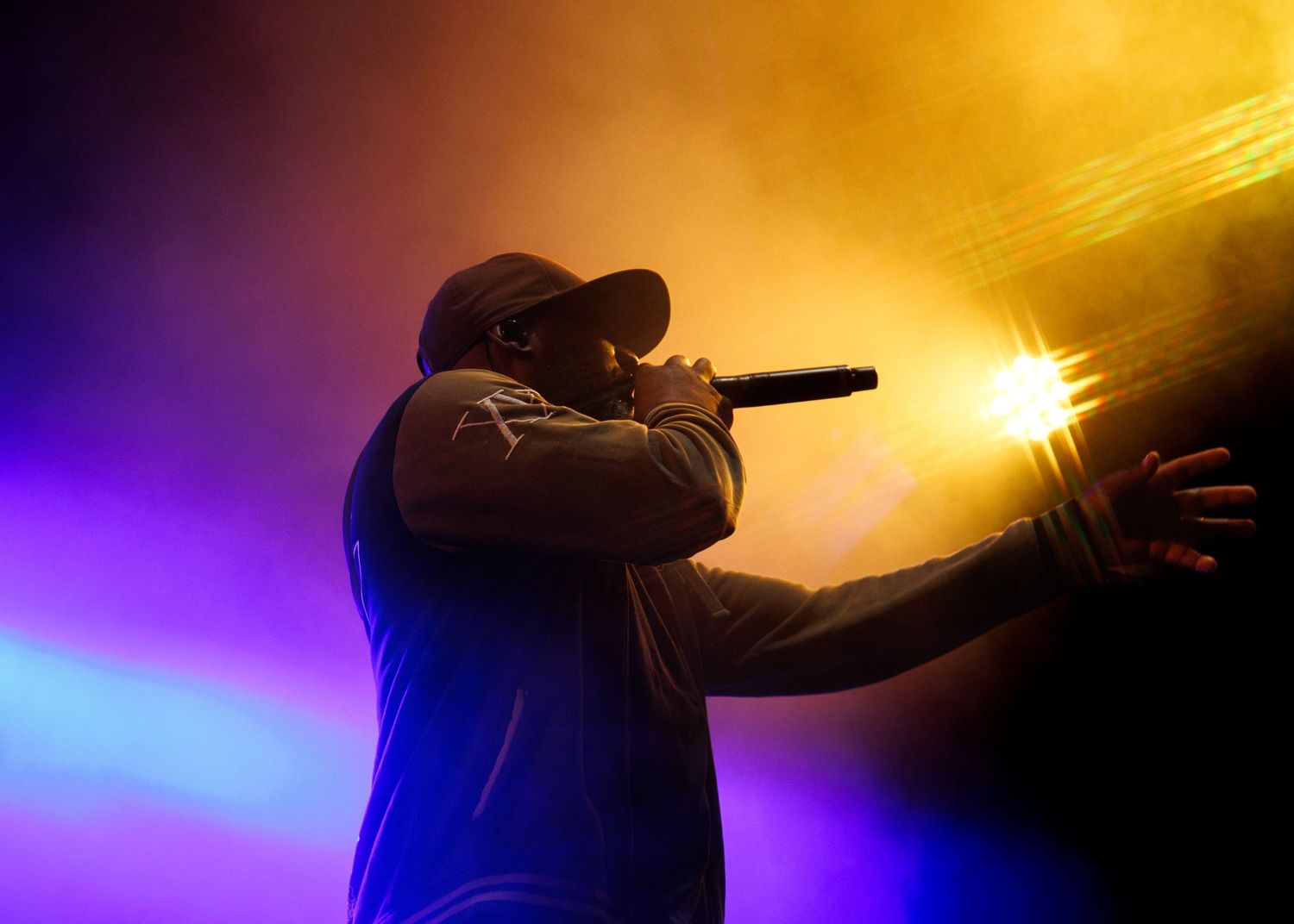 Silhouetted performer on stage illuminated by dramatic orange and purple concert lighting effects.