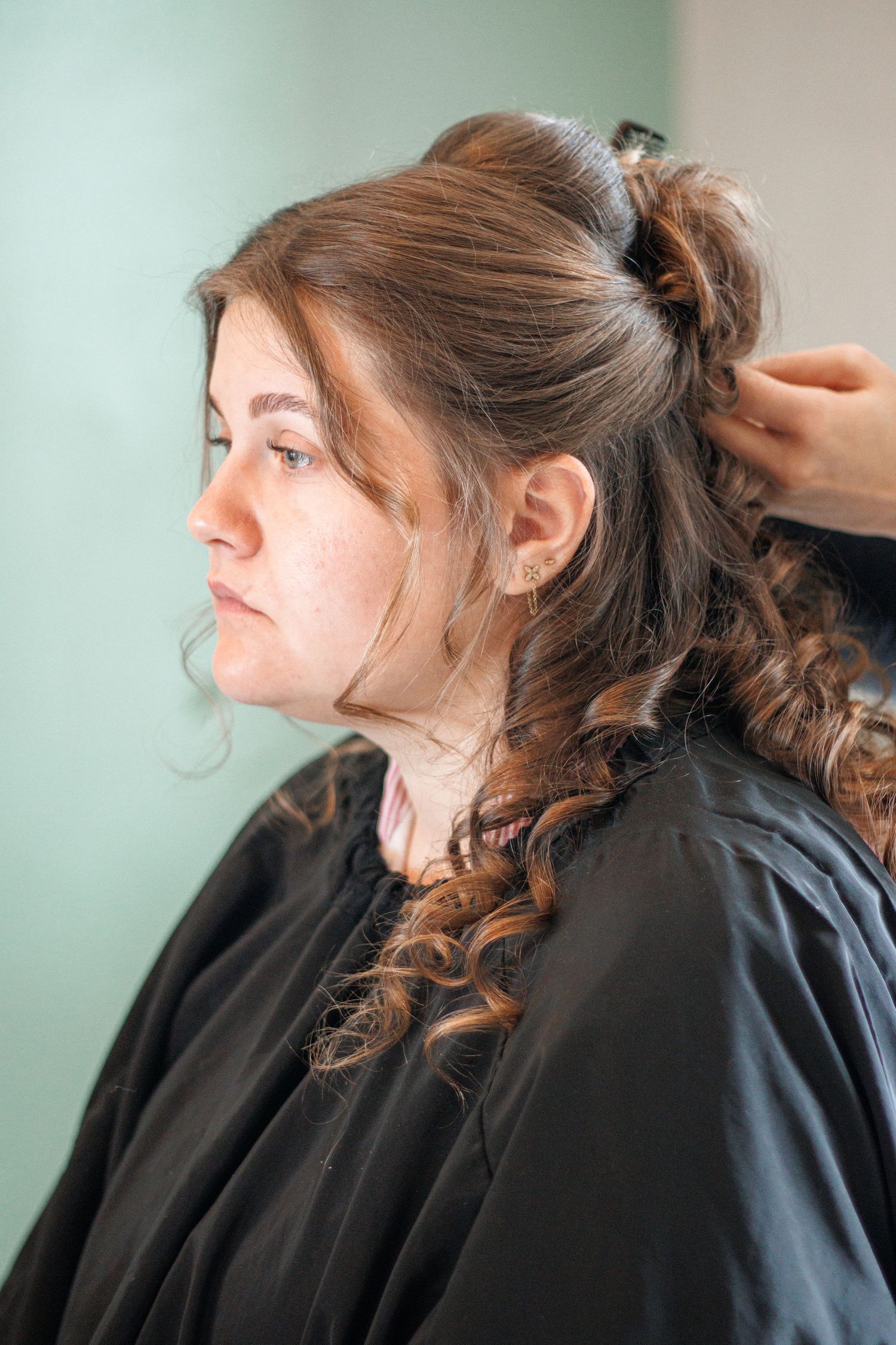 Woman in black salon cape getting curly hair styled by hairdresser in a beauty salon.