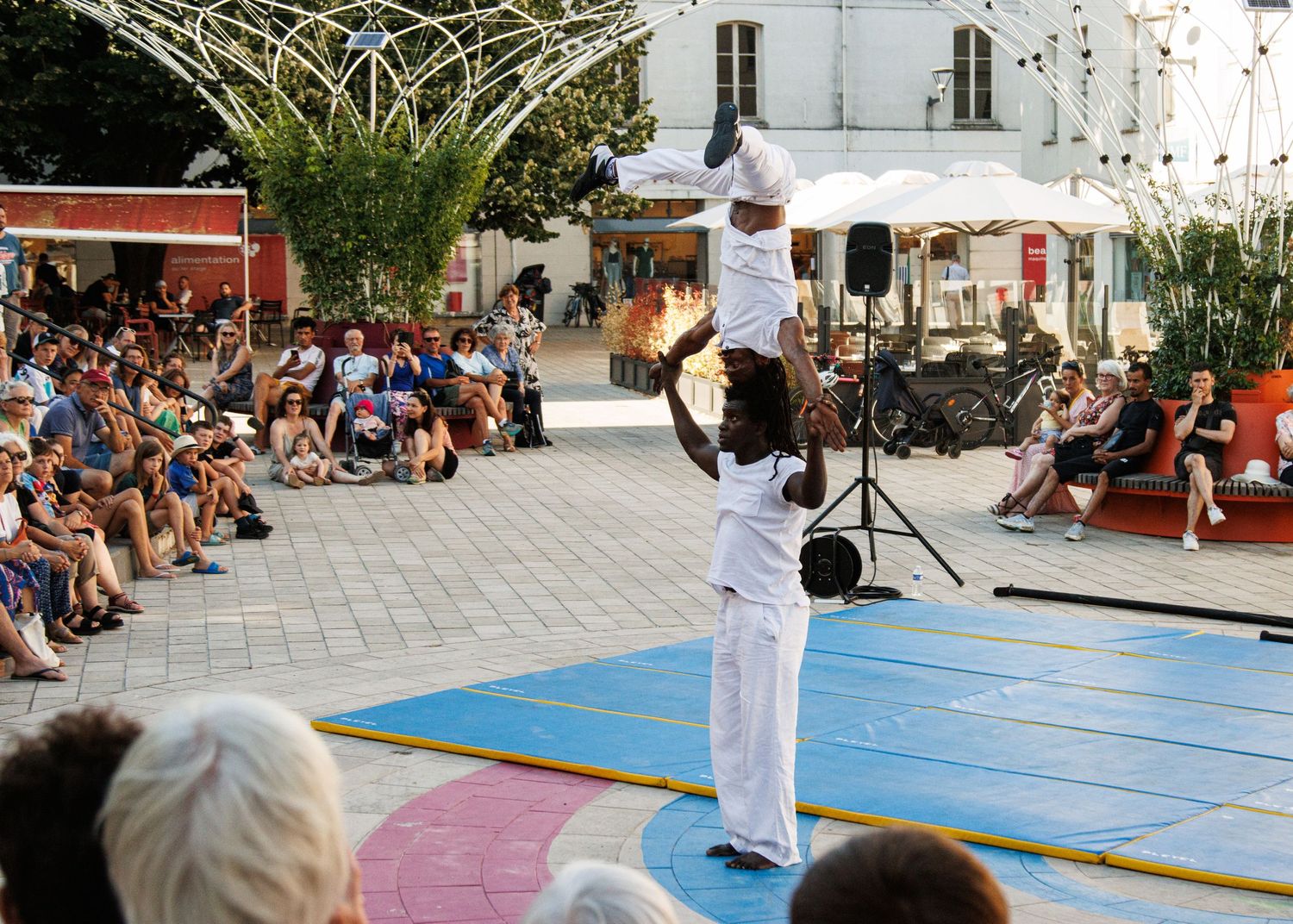 Street performers demonstrate skilled acrobatic moves on outdoor stage with palm trees in background.