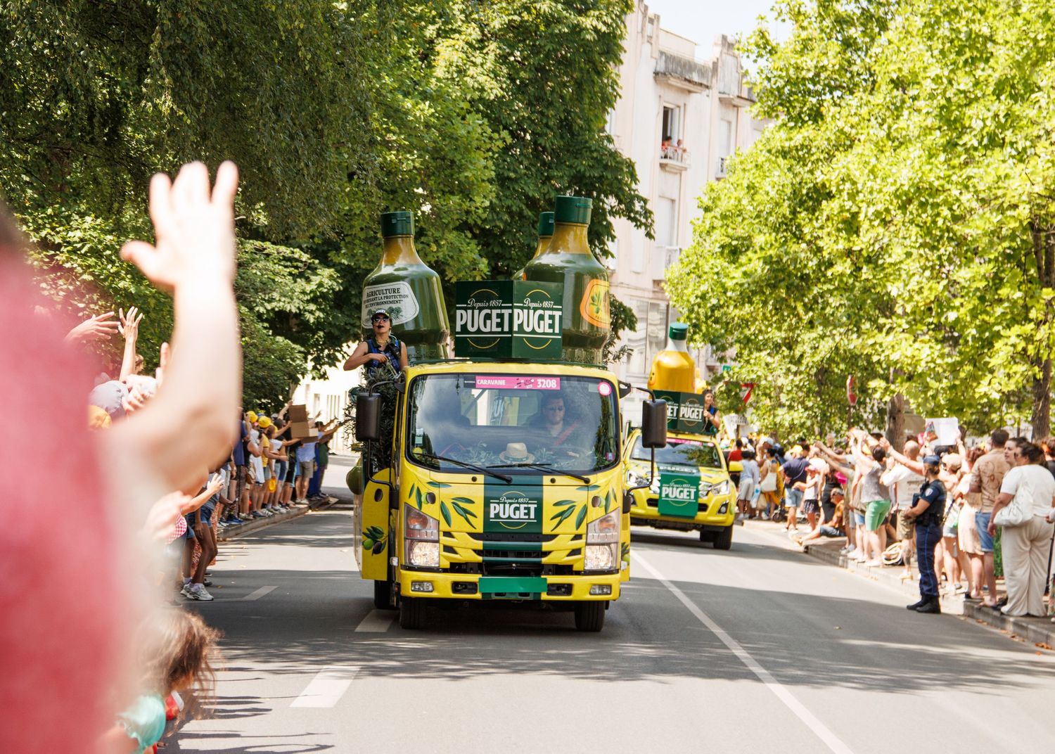 Green promotional truck driving through street parade with waving spectators.