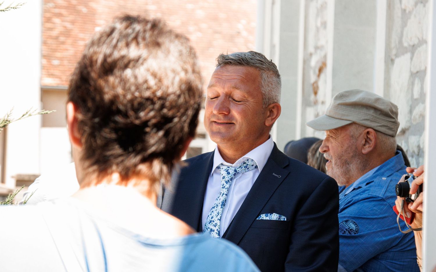 A gathering of people conversing outdoors near a white columned building.