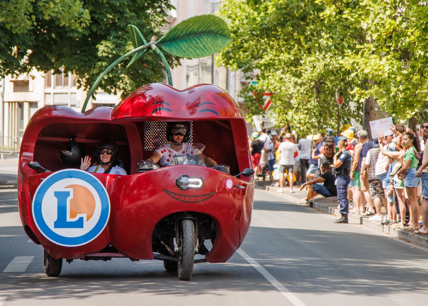A red novelty vehicle shaped like a large scooter drives in a promotional parade.