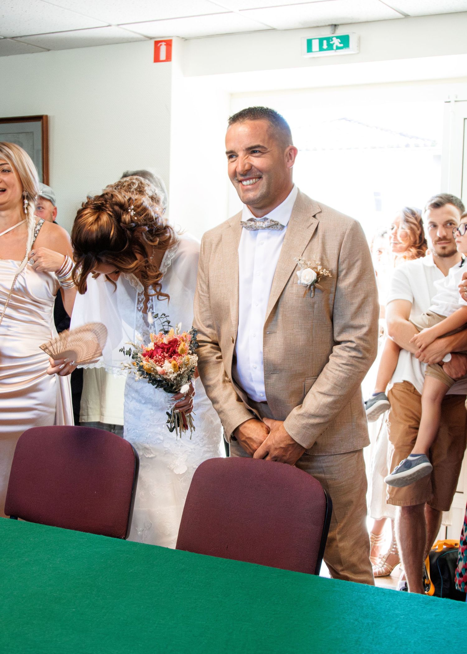 A joyful moment at a civil ceremony with people standing by a green table, including someone wearing a beige suit.