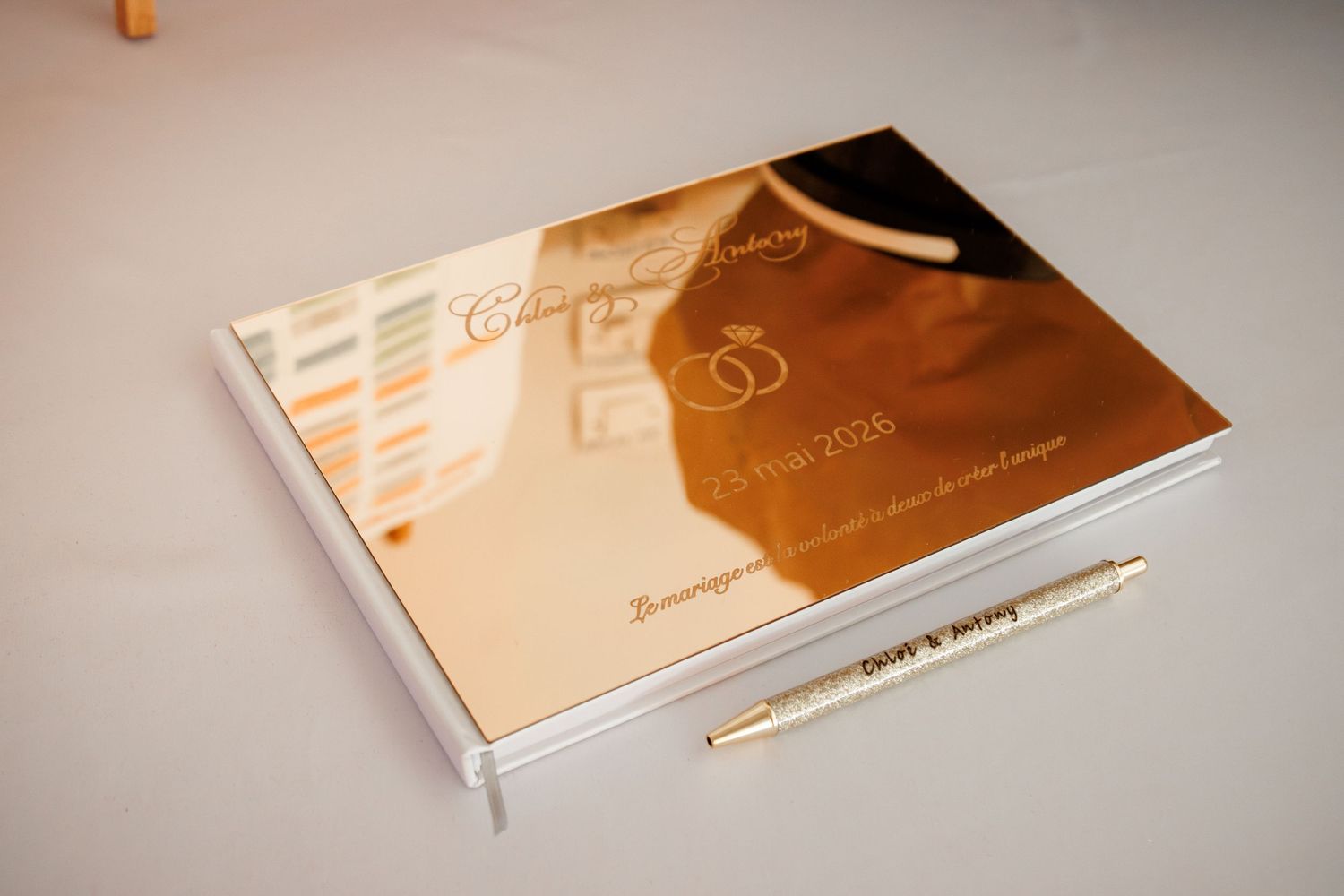 Gold mirrored wedding guest book with a personalized pen on a white table at a wedding reception.