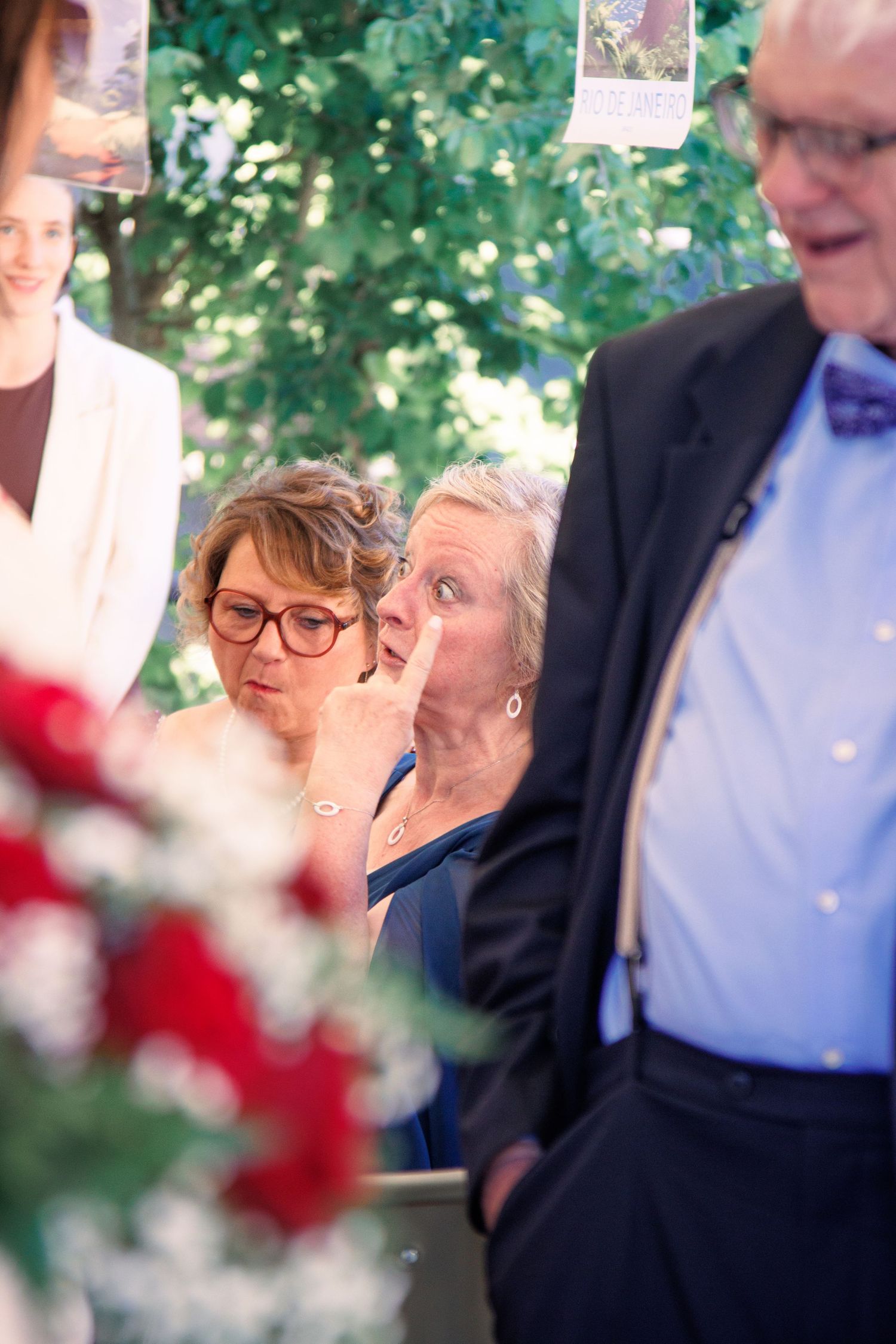 Emotional wedding guests wiping tears during an outdoor ceremony with red floral decorations.