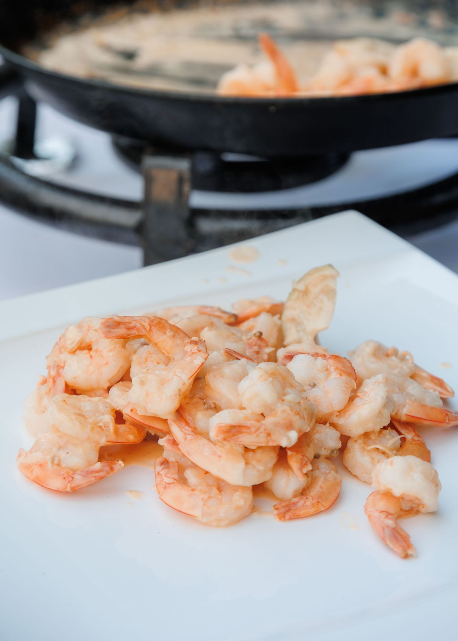 Pile of freshly cooked pink shrimp on a white cutting board with a paella pan in the background.