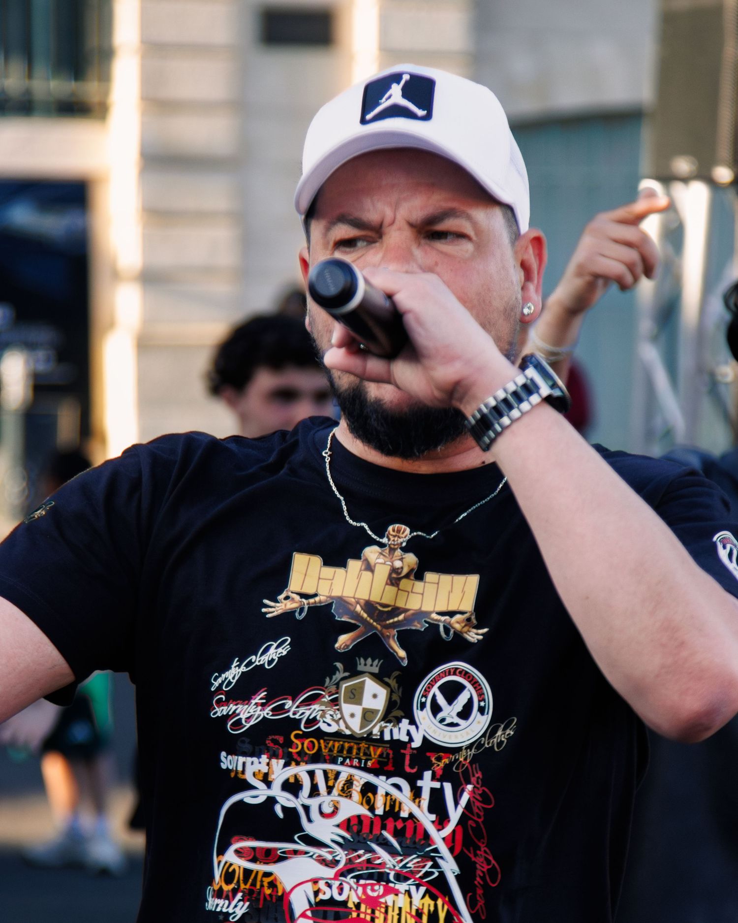Performer in black shirt and Jordan cap sings into microphone during outdoor show.