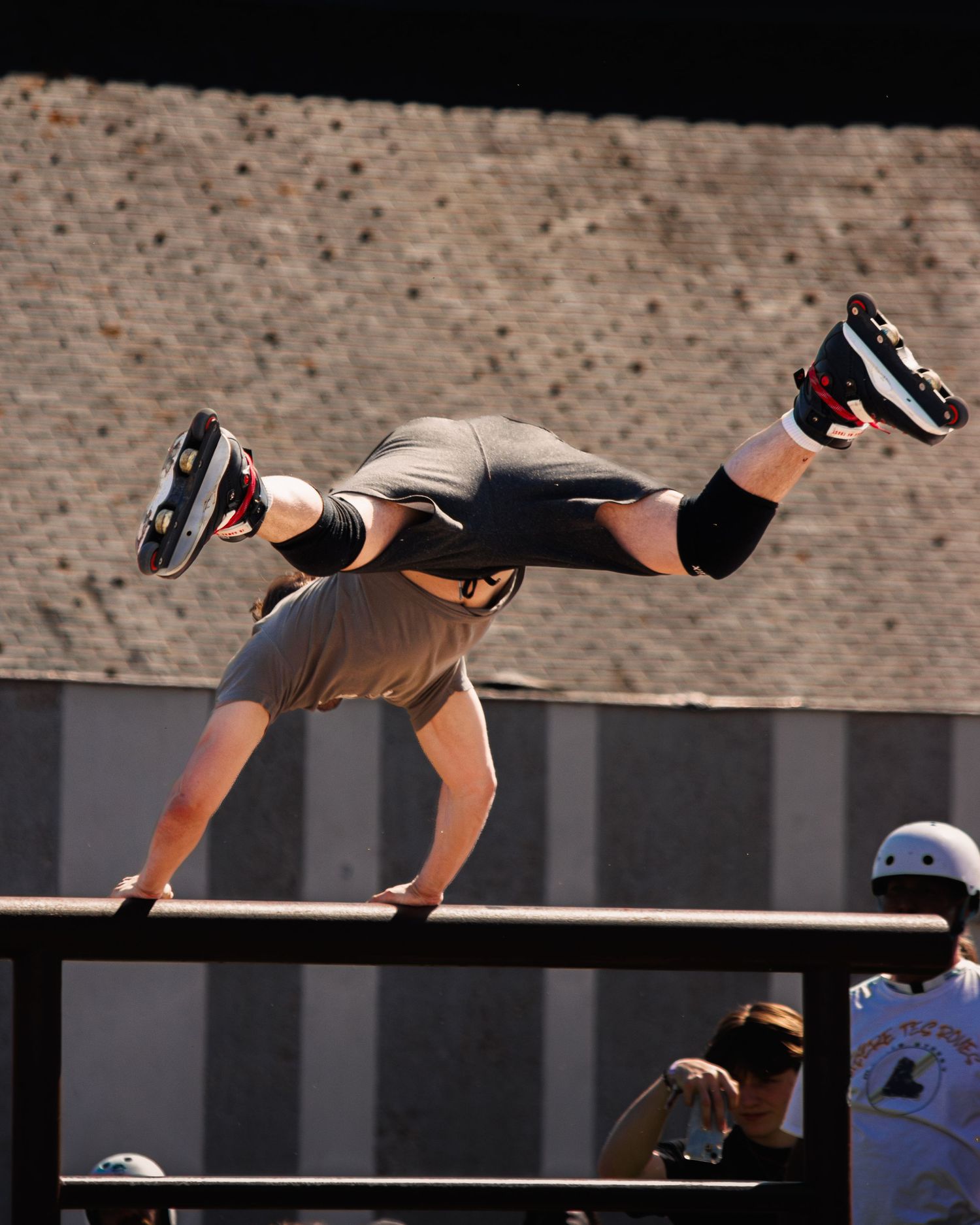 BMX rider performs skillful aerial trick over black railing against brick wall backdrop.