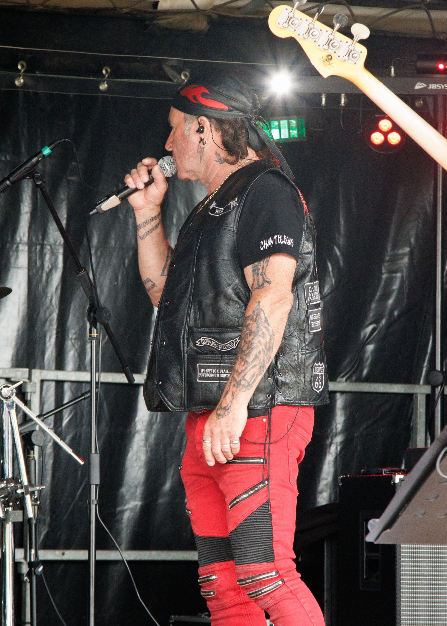 Rock performer in red pants and leather vest singing on stage with concert lighting.