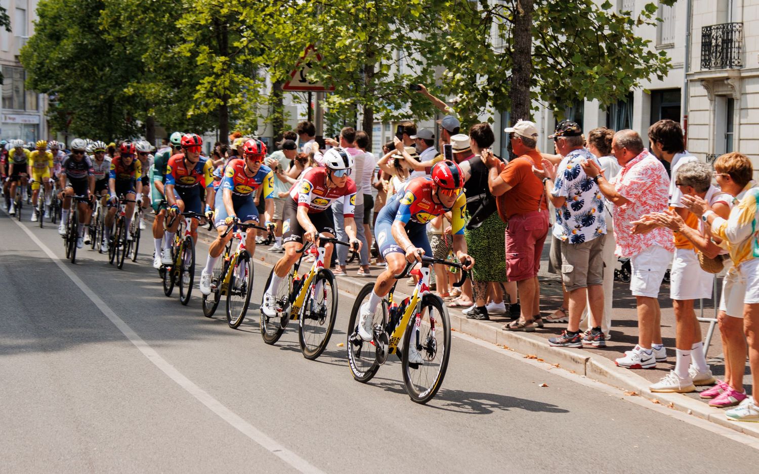 Cyclists in colorful jerseys compete in a road race as crowds gather along the route to watch.