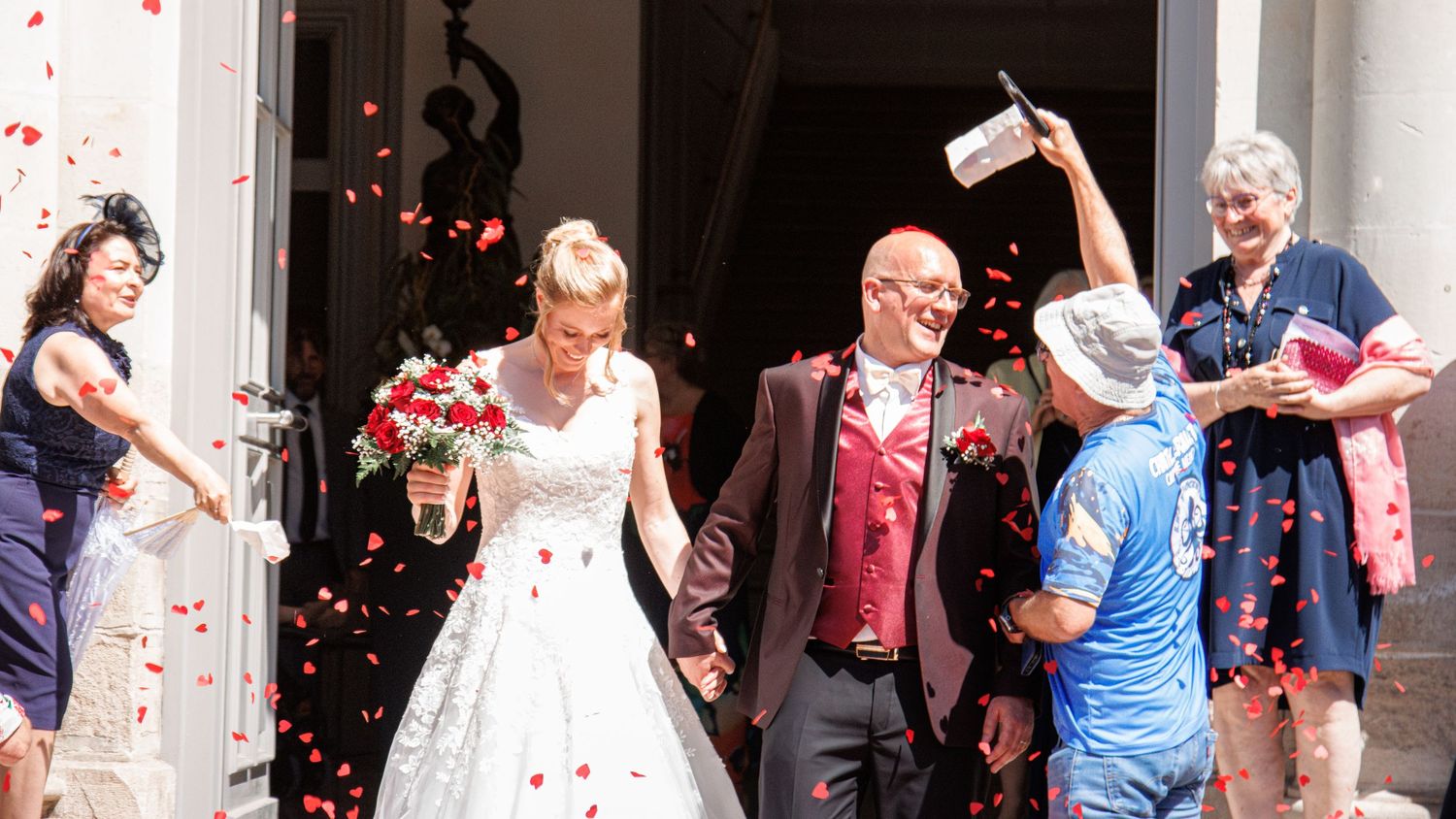 Joyful newlyweds exit a church entrance as guests shower them with red rose petals in celebration.
