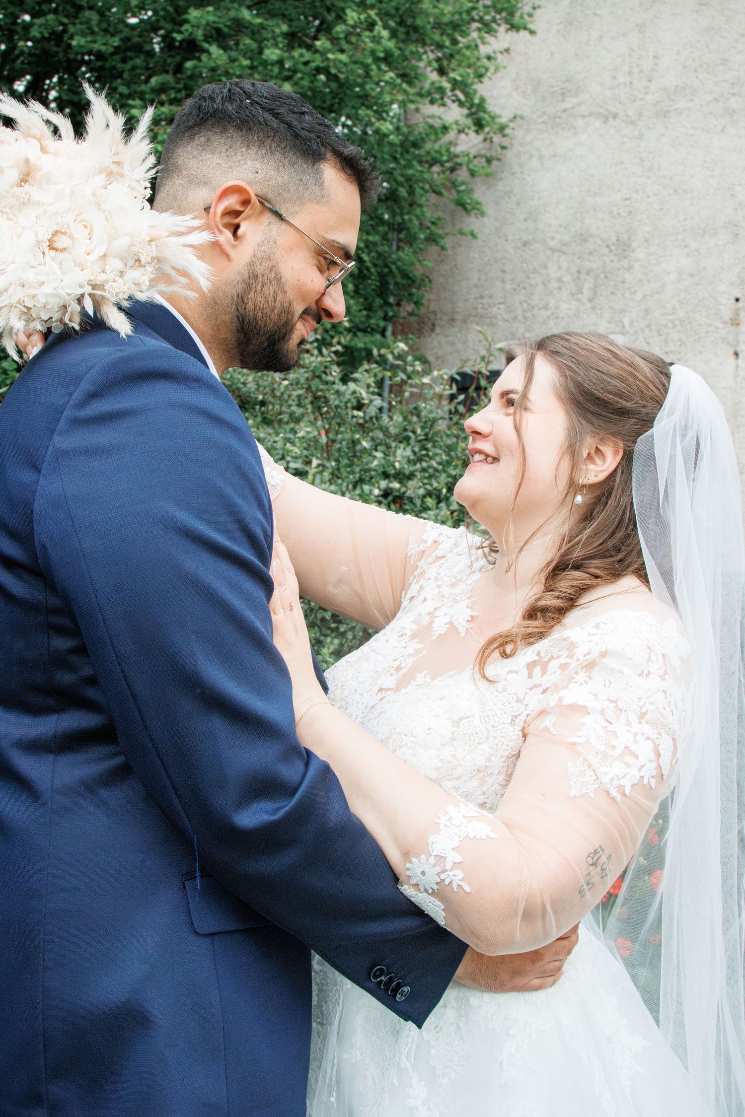 A bride and groom share a joyful moment, smiling at each other, she in lace gown with veil, he in navy suit.