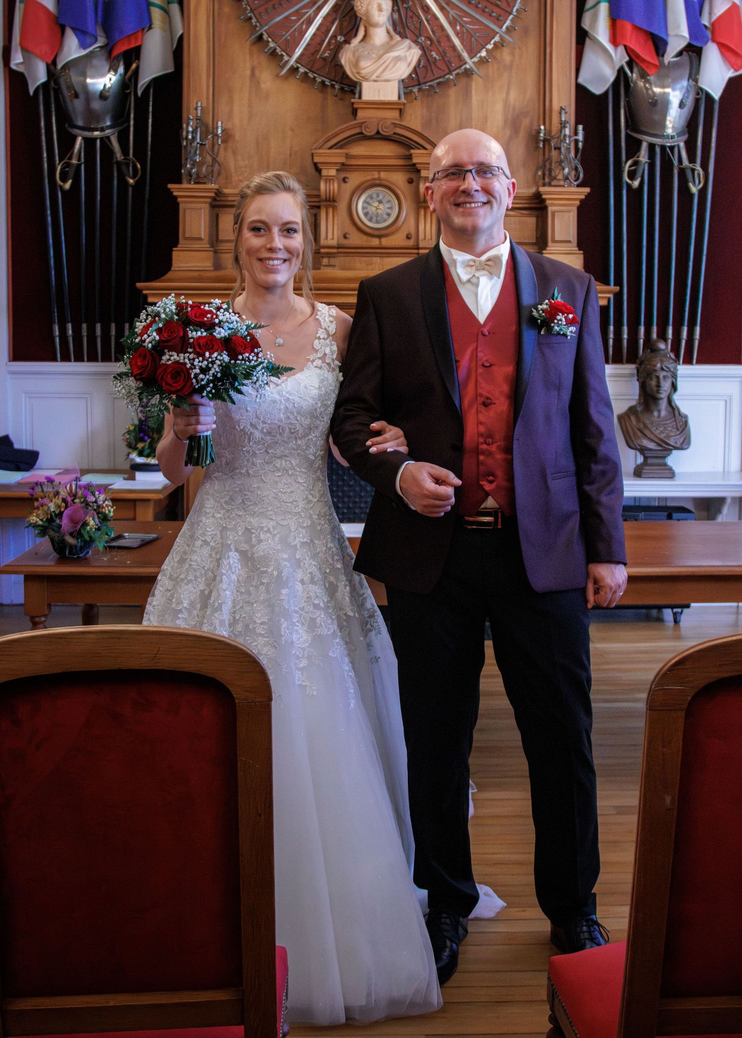 Bride and groom smiling together at wedding ceremony in ornate hall with flags and armor decorations.
