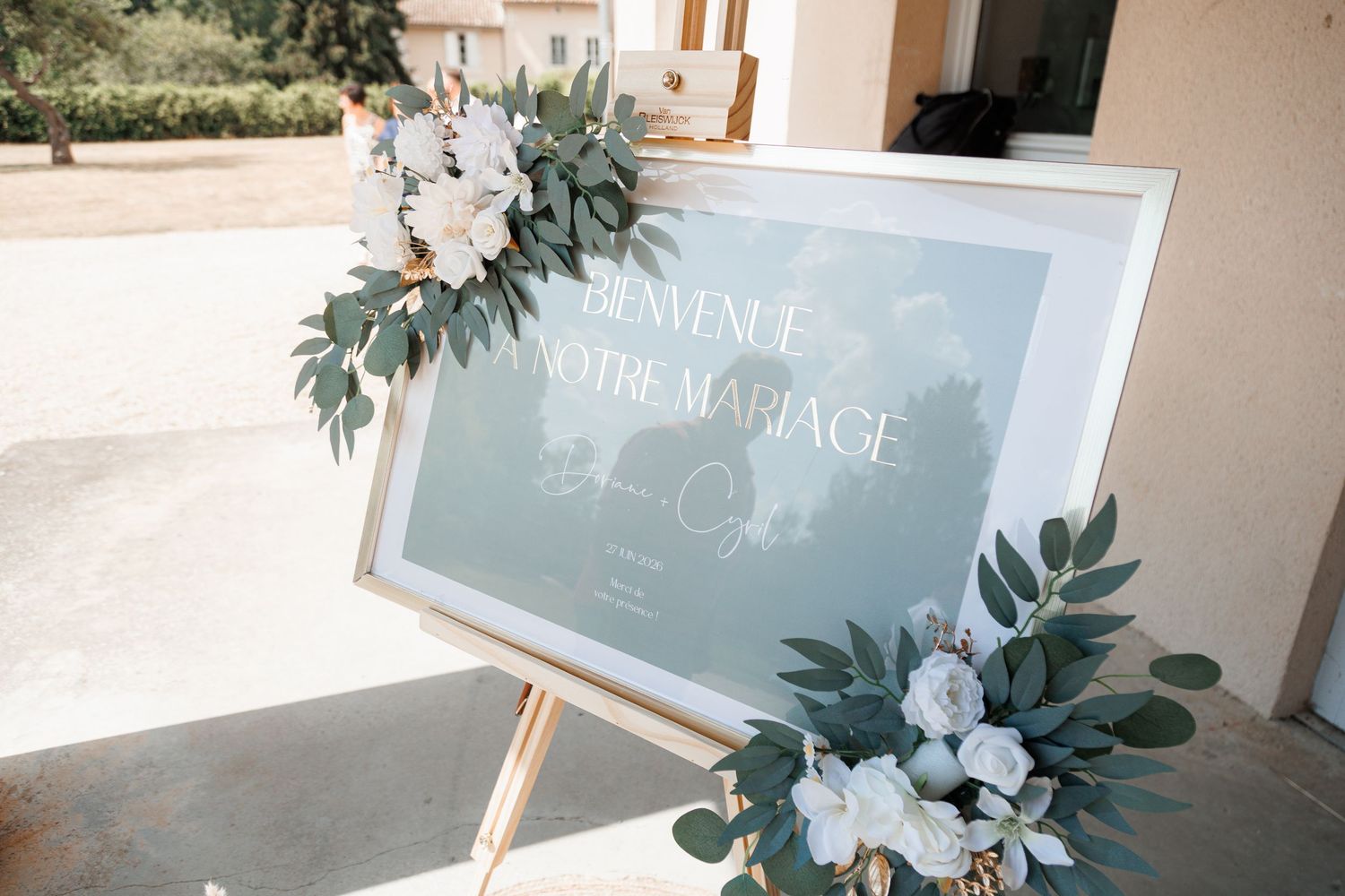 Elegant wedding welcome sign reading Bienvenue a Notre Mariage decorated with white roses and eucalyptus.