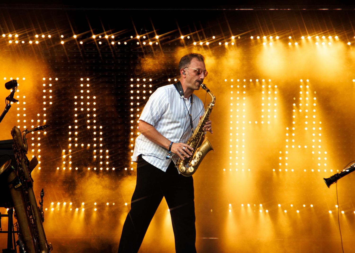 Saxophonist performing on stage with dramatic golden lighting and illuminated letters backdrop at live concert.