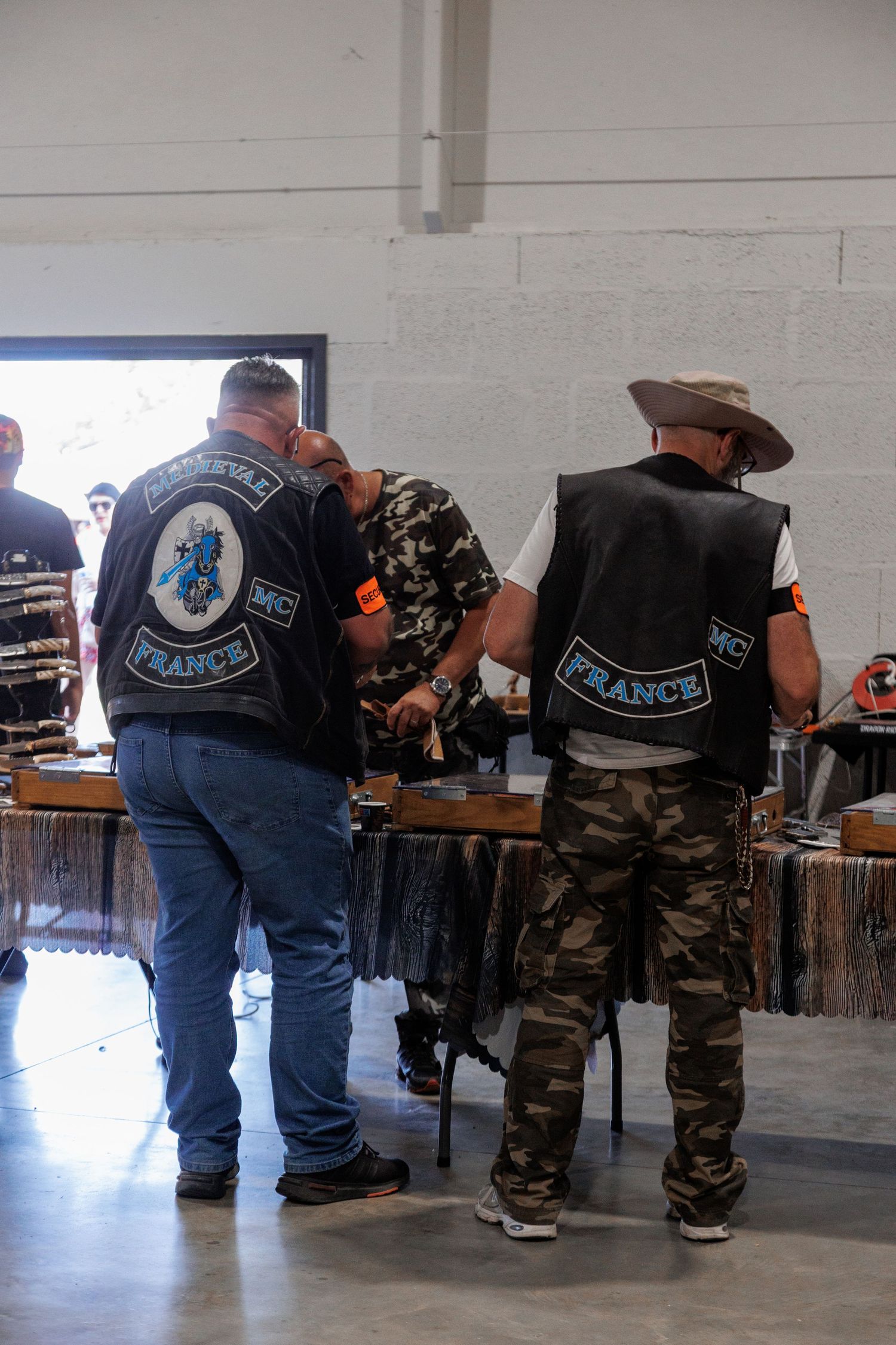 Members of France MC biker club in leather vests browse merchandise at an indoor motorcycle rally event.